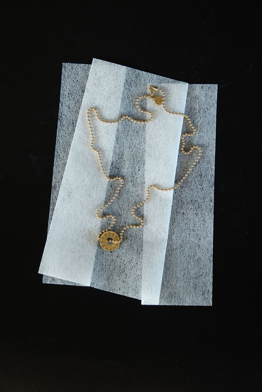 Gold pendant necklace arranged on translucent white paper against a black background