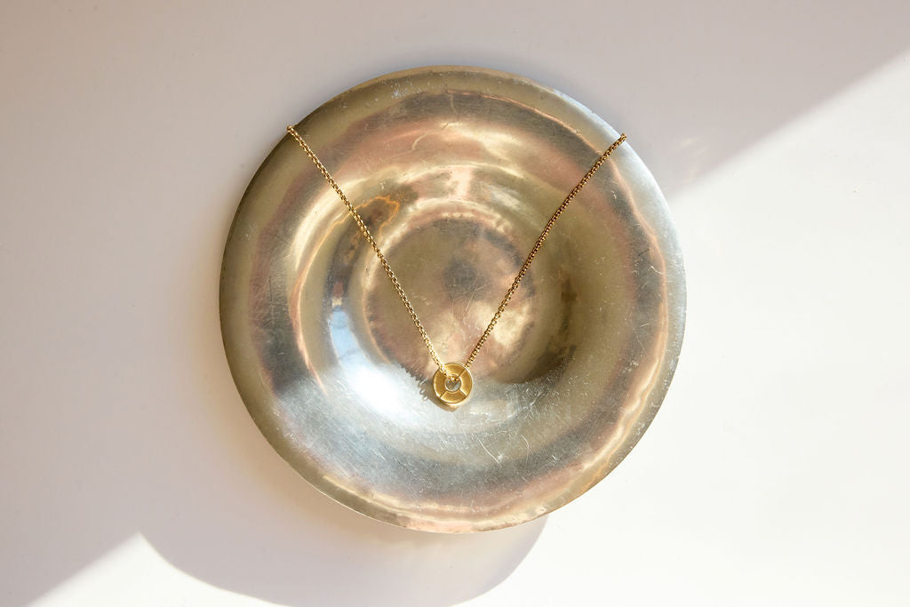 Gold pendant necklace photographed on a reflective brass bowl