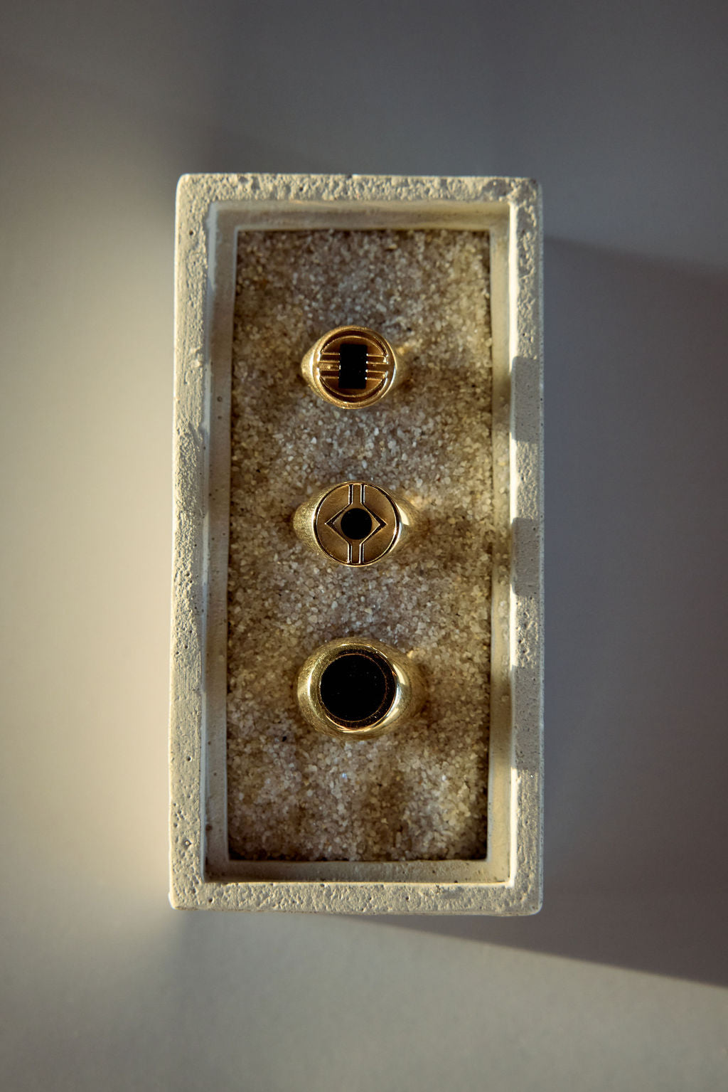 Three gold signet rings with black stone inlays displayed in a textured tray